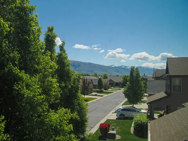 Neighborhood setting featuring residential properties, mature trees, and a street with parked vehicles