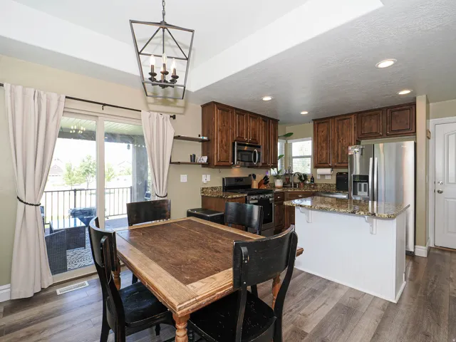 Kitchen and dining area featuring wood-finish flooring, dark wood cabinetry, granite countertops, and stainless steel appliances