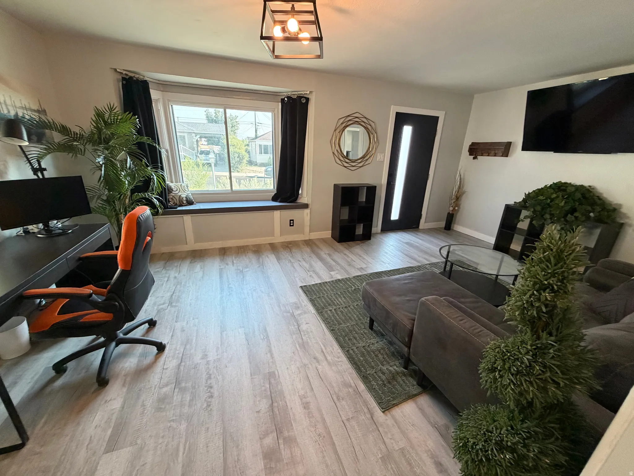 Window seat with storage, light wood-finish flooring, modern ceiling fixture, black entry door with frosted glass insert, and neutral wall paint