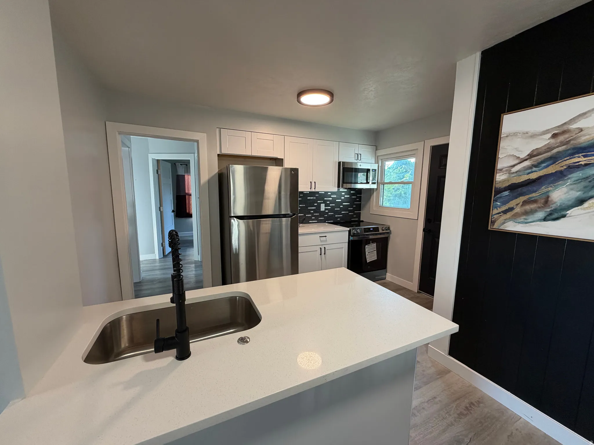Kitchen featuring stainless steel appliances, white cabinetry, dark subway tile backsplash, and light-colored countertops