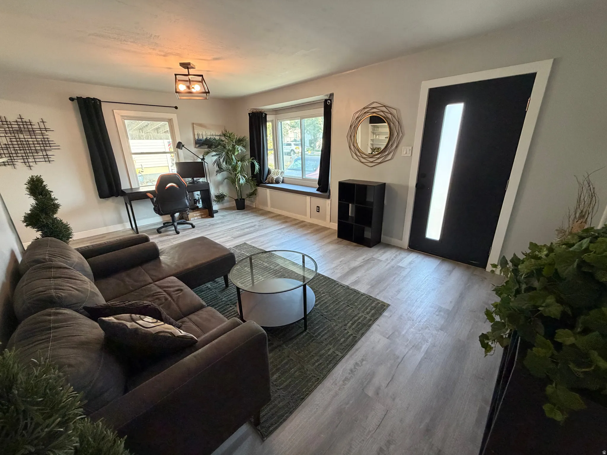 Wood-finish flooring throughout, featuring a bay window with a built-in bench, and a modern black entry door with a vertical glass insert