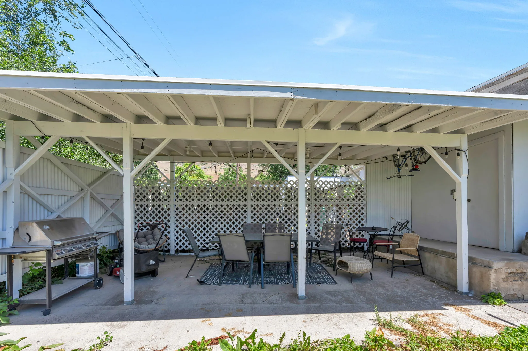 Covered patio with a concrete slab, white lattice privacy screens, and exposed beam ceiling