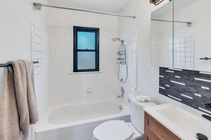 Bathroom featuring white subway tile, a dark-framed window, a modern vanity with a white countertop, and a textured black and white tile accent wall