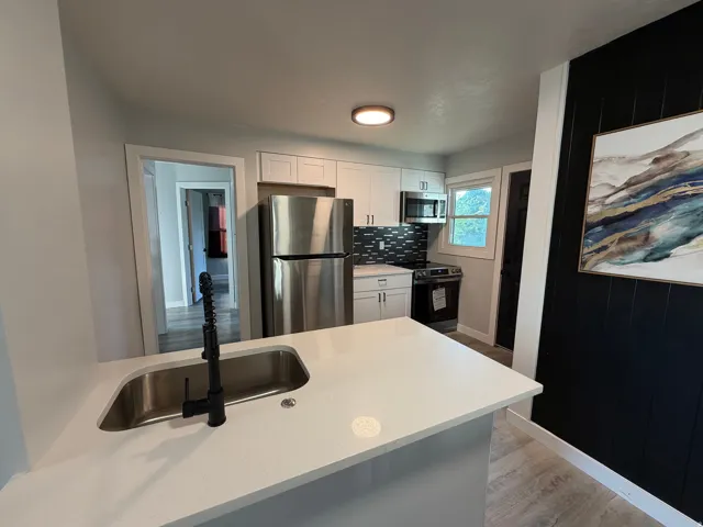 Kitchen featuring stainless steel appliances, white cabinetry, dark subway tile backsplash, and light-colored countertops