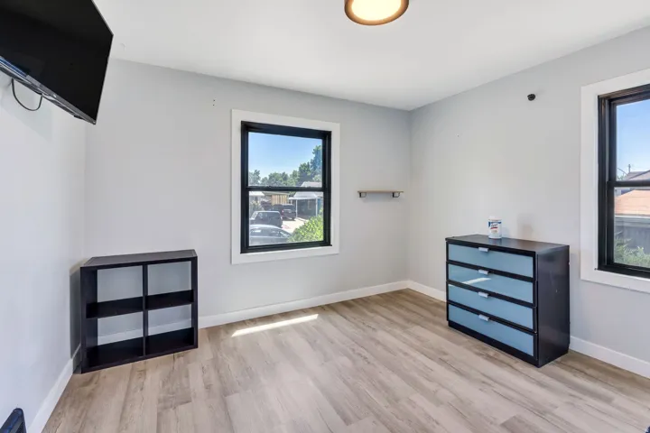 Room featuring light wood-finish flooring, two large windows with black frames, and light gray painted walls