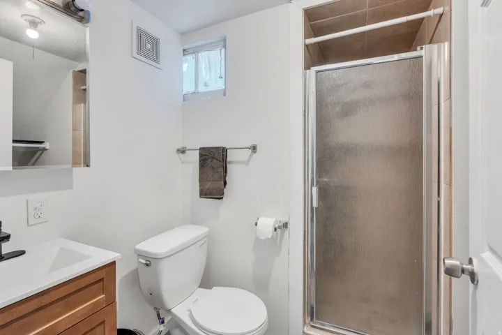 Bathroom featuring a single vanity with wood-finish cabinetry, a white countertop, a rectangular sink, and shower.