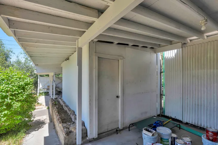 Covered outdoor area featuring exposed ceiling joists, an exterior door, and corrugated metal siding