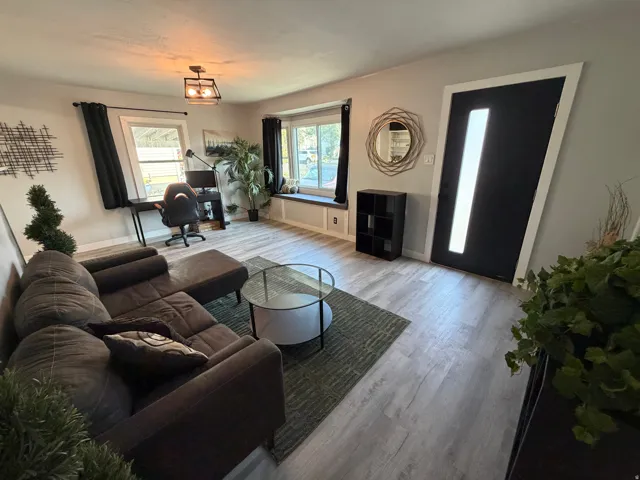 Wood-finish flooring throughout, featuring a bay window with a built-in bench, and a modern black entry door with a vertical glass insert