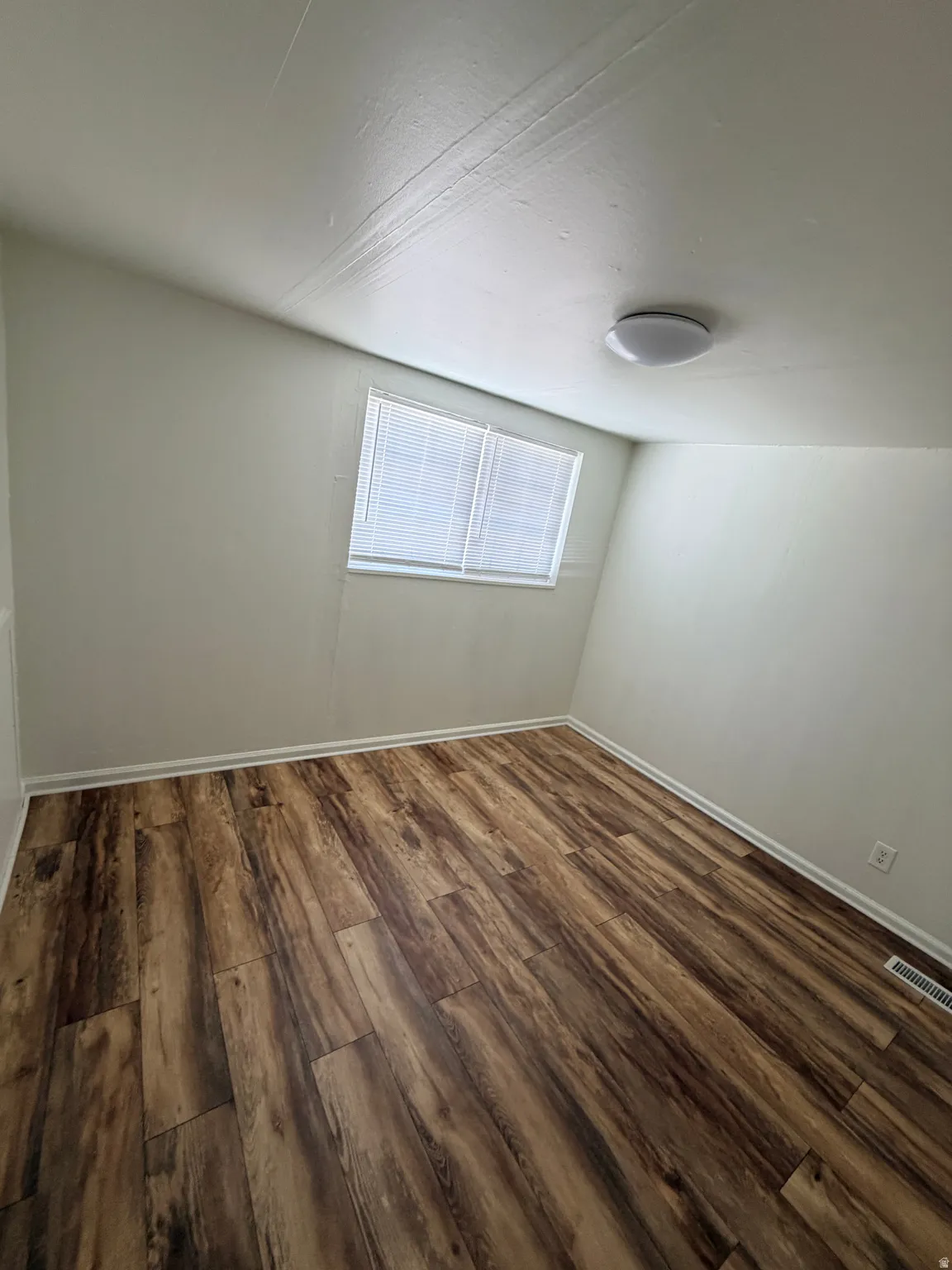 Room featuring wood-finish flooring, white baseboards, a single window with blinds, and a flush-mount ceiling light fixture