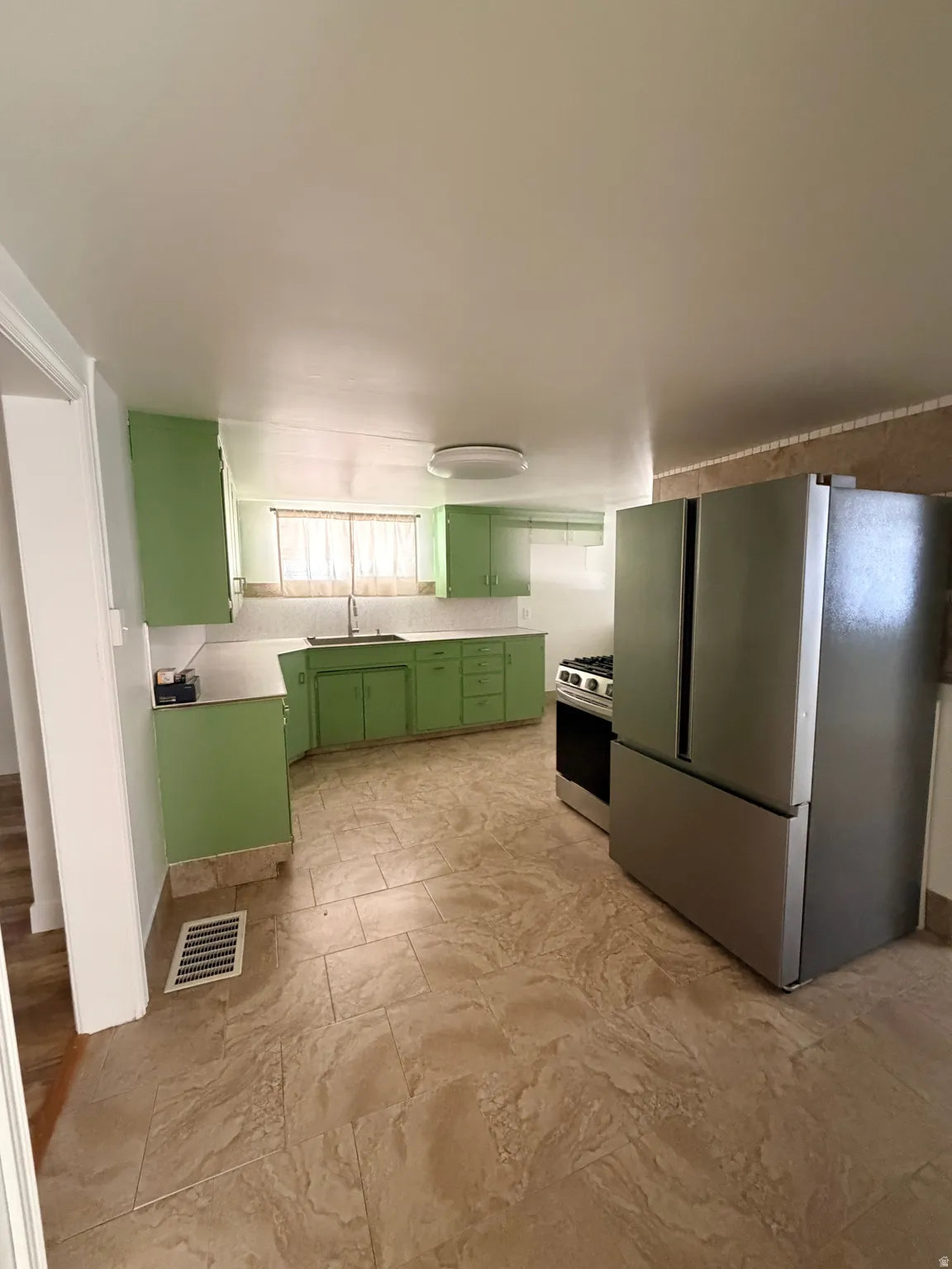 Kitchen featuring light green cabinetry, a stainless steel refrigerator, a stainless steel range, a window above the sink, and patterned tile flooring