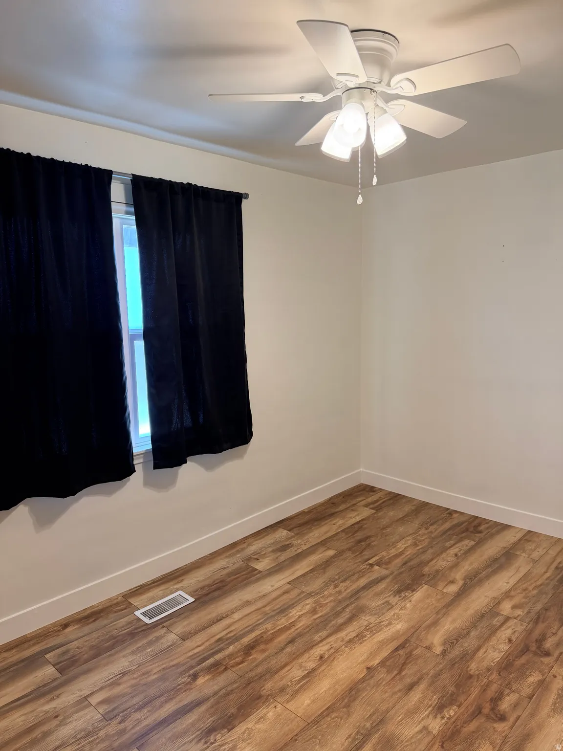 Room featuring wood-finish flooring, white walls, and a window with a curtain rod