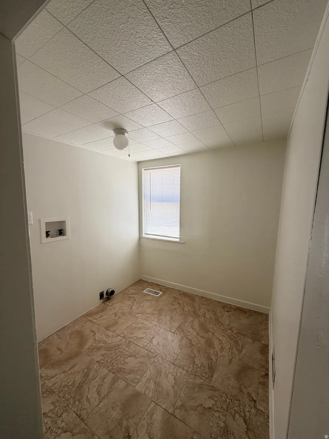 Utility room featuring durable tile-style flooring, a single window with blinds, and a surface-mounted ceiling light fixture