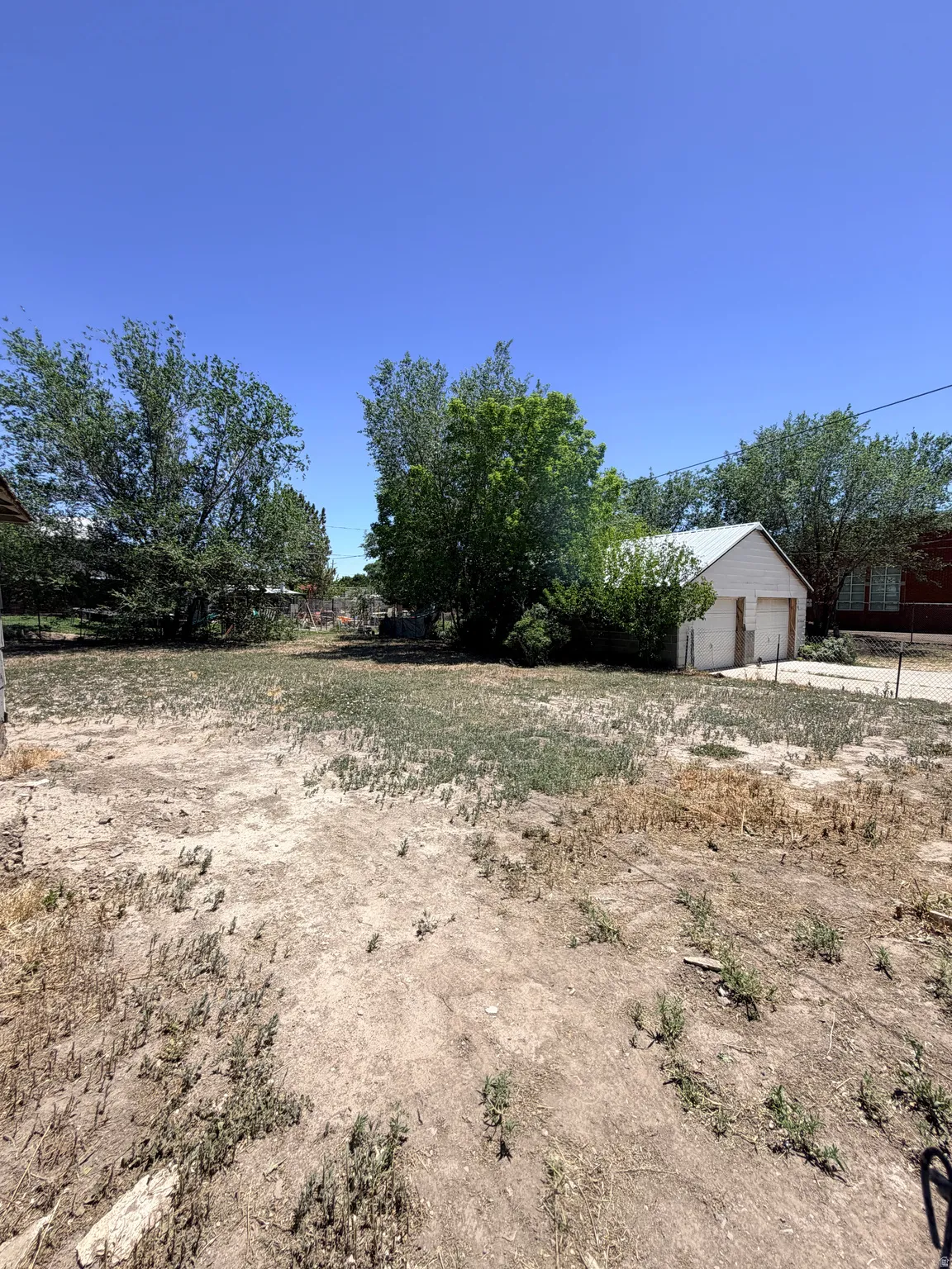 Expansive rear yard with a detached garage structure, mature trees, and open-air space