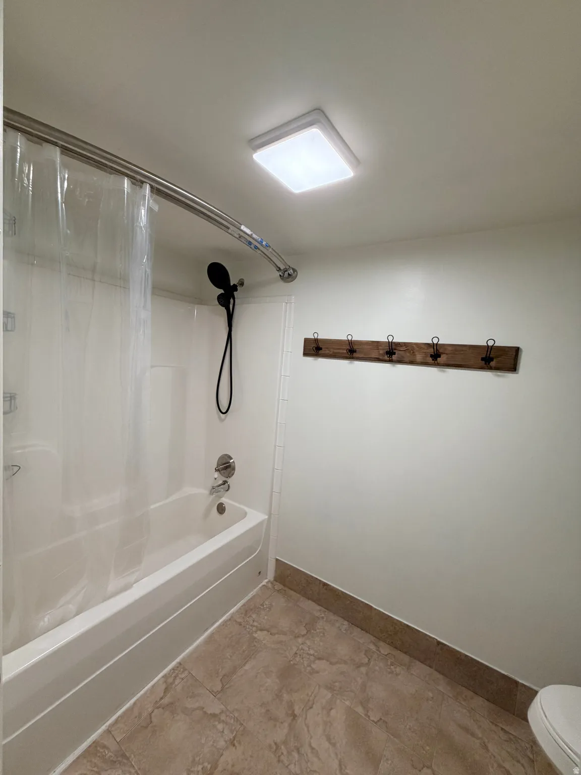 Bathroom featuring a white bathtub with a curved shower rod, a wall-mounted showerhead with handheld attachment, and a tiled shower surround