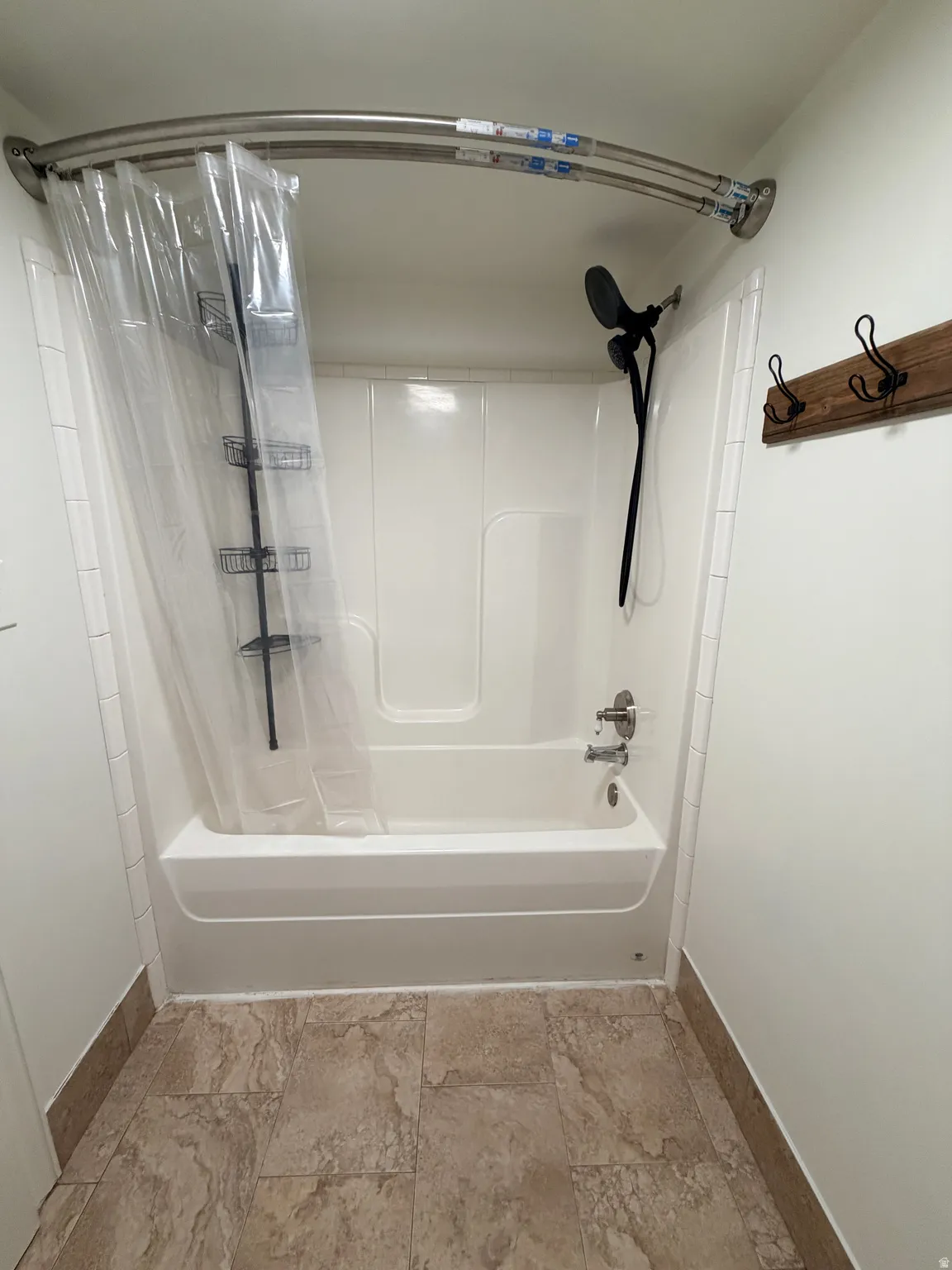 Bathtub and shower combination featuring a white surround and a black wall-mounted showerhead