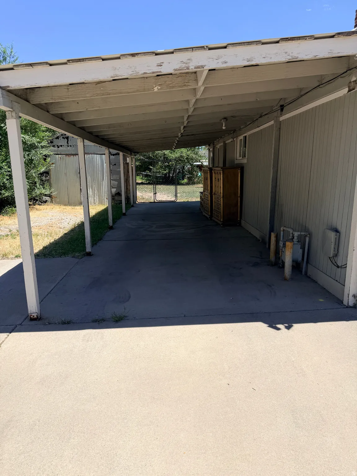 Extended carport with concrete flooring, supported by white posts, leading to an open backyard area