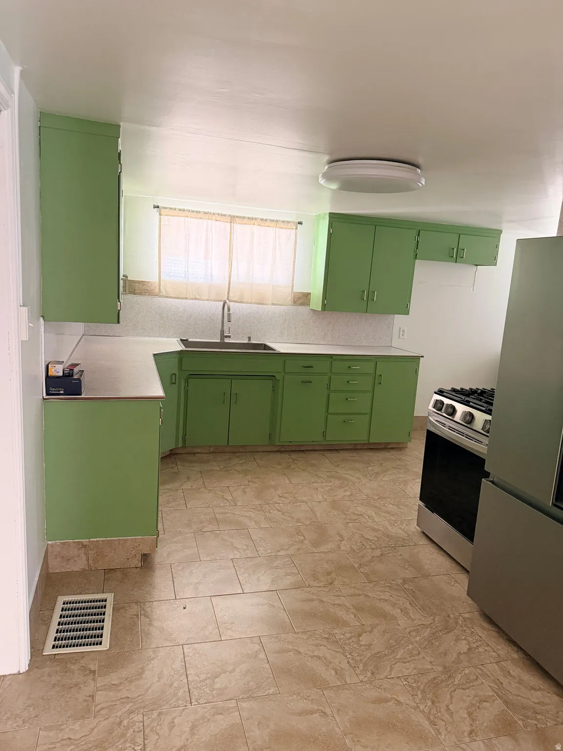 Kitchen featuring green cabinetry, light-toned countertops, a stainless steel gas range, and large format floor tiling