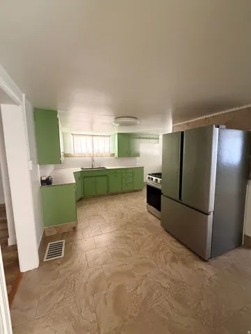 Kitchen featuring light green cabinetry, a stainless steel refrigerator, a stainless steel range, a window above the sink, and patterned tile flooring