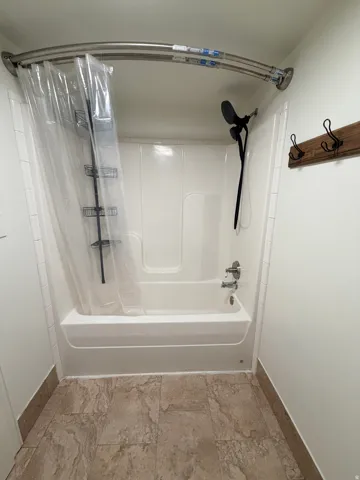 Bathtub and shower combination featuring a white surround and a black wall-mounted showerhead