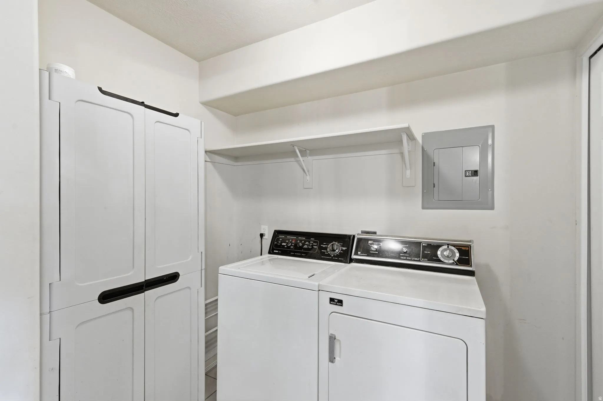 Dedicated laundry room with a white washing machine and dryer, a built-in wall shelf for storage, and a utility cabinet with dark handles