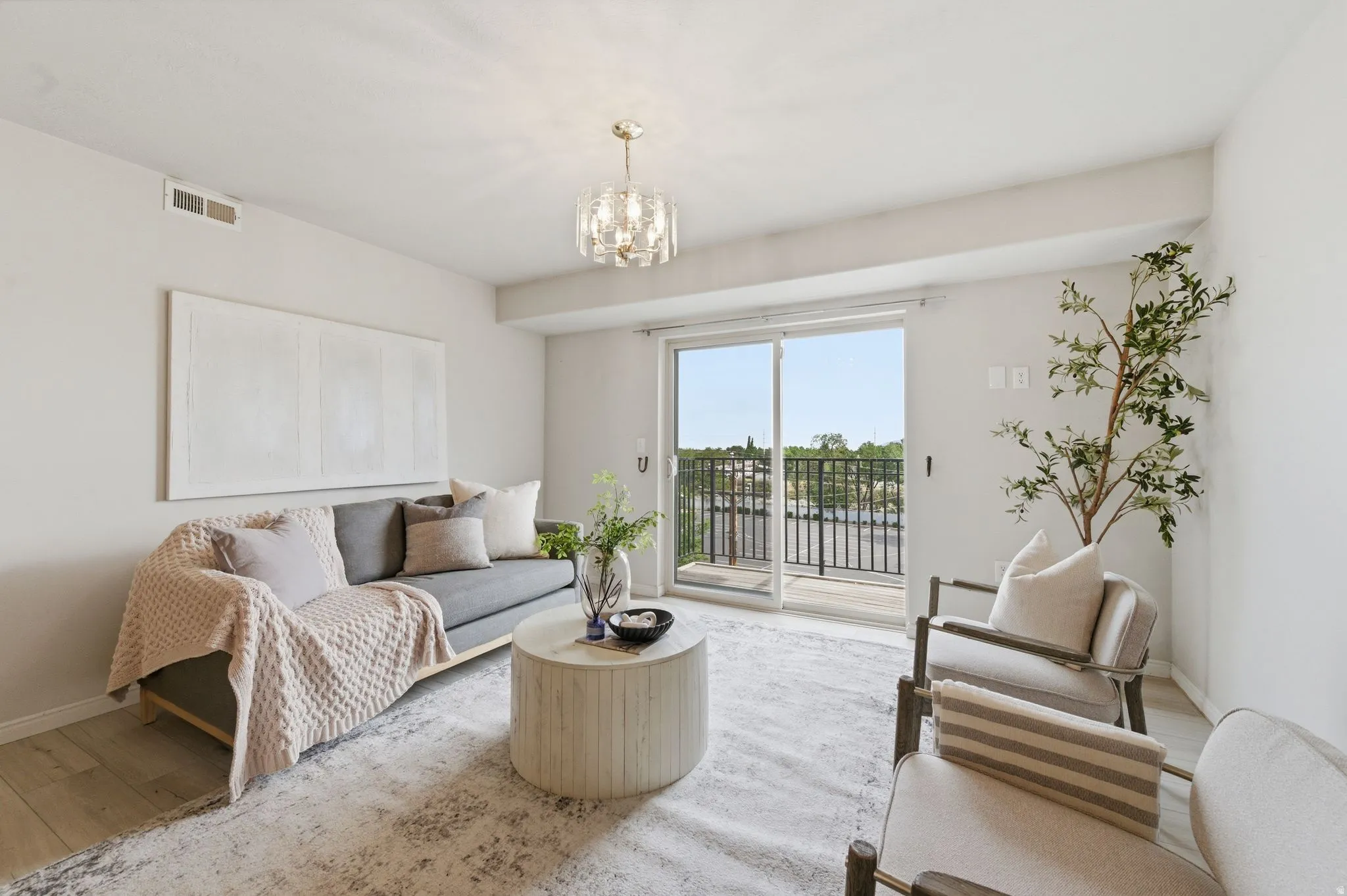 Bright living space featuring light wood-finish flooring, a contemporary chandelier, and direct access to an outdoor balcony through sliding glass door