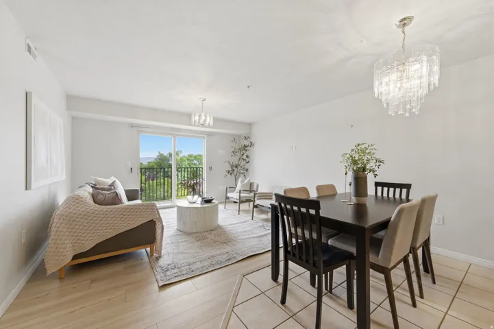 Open-concept living and dining area featuring wood-finish flooring, a contemporary chandelier, and a sliding glass door opening to a balcony