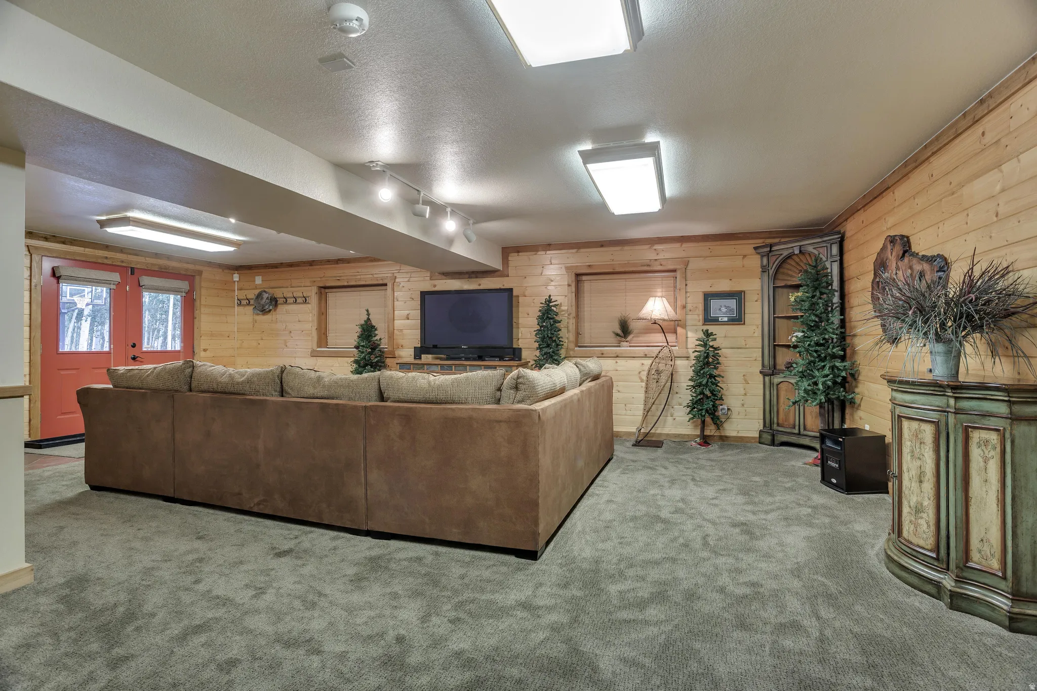 Spacious room featuring carpet flooring, horizontal wood paneling on walls, recessed lighting, and a double-door entry with a red finish