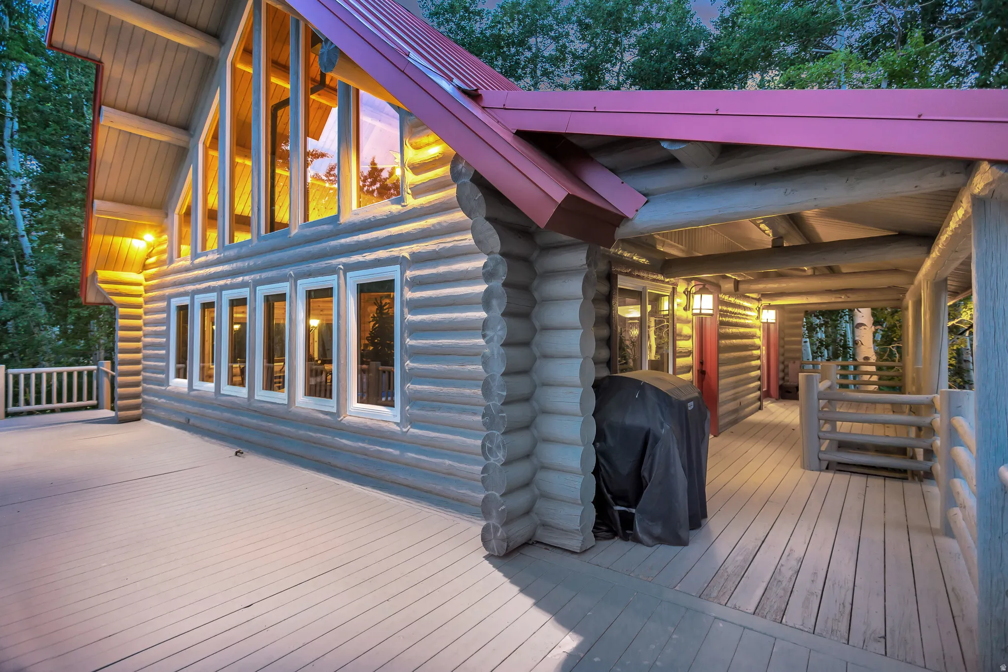 Log cabin exterior featuring a red metal roof, full-length windows, and a wrap-around porch with wooden railing