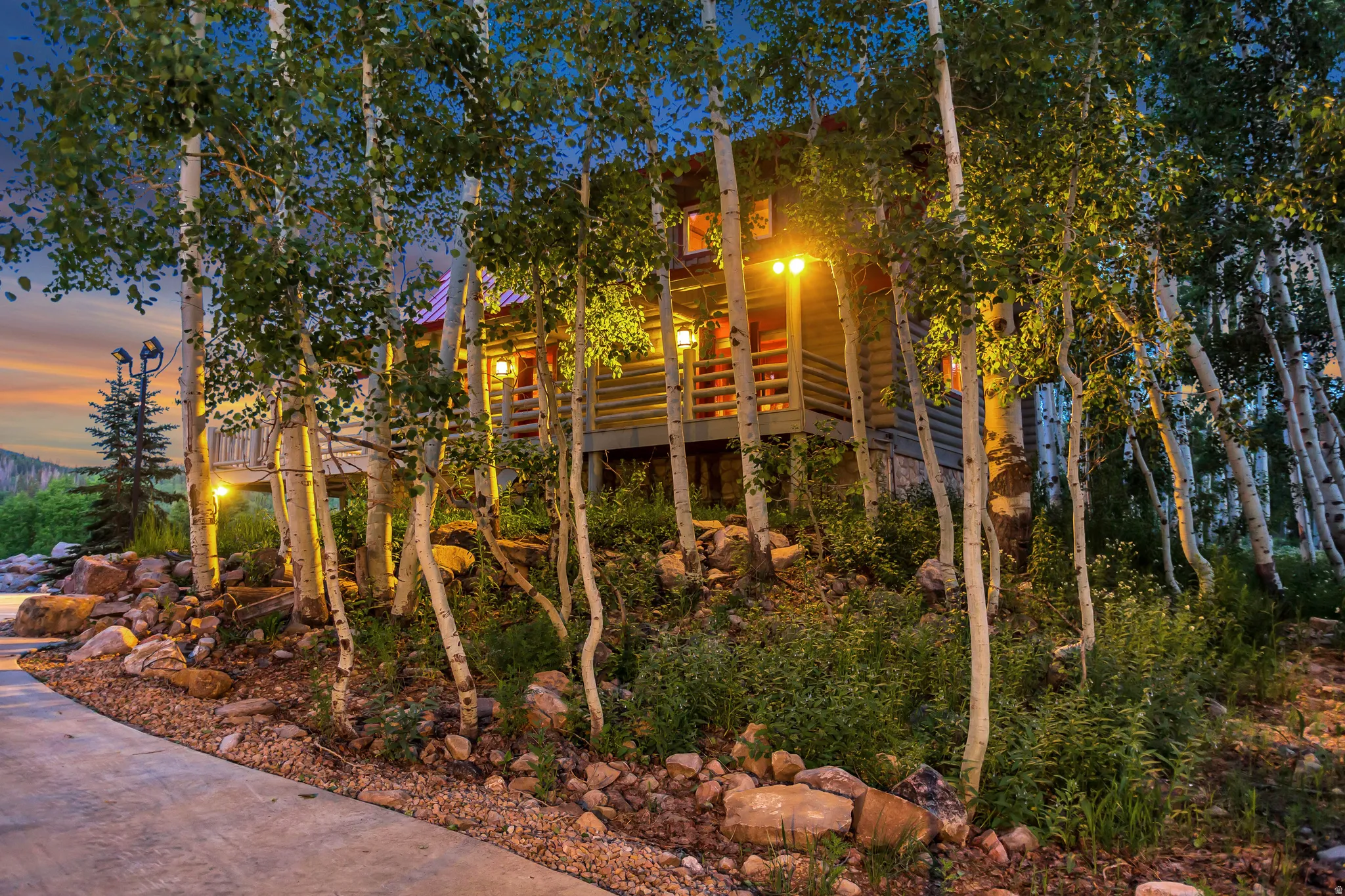 Log cabin exterior featuring a raised deck, surrounding aspen trees, and integrated exterior lighting