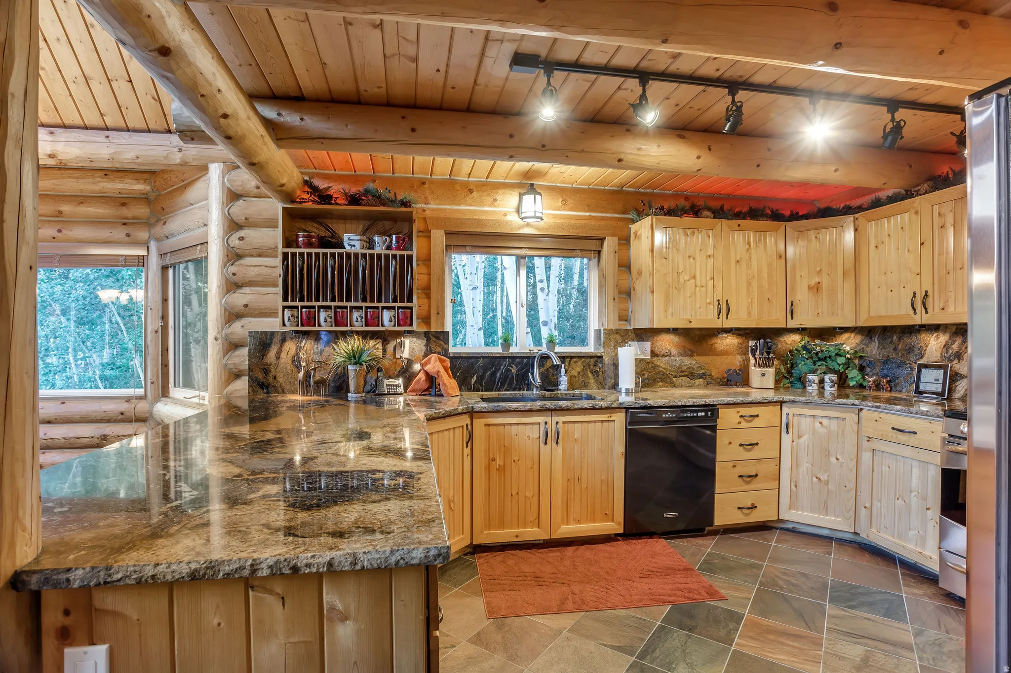 Rustic kitchen featuring log construction, wood-finish cabinetry, stone slab countertops, and slate flooring