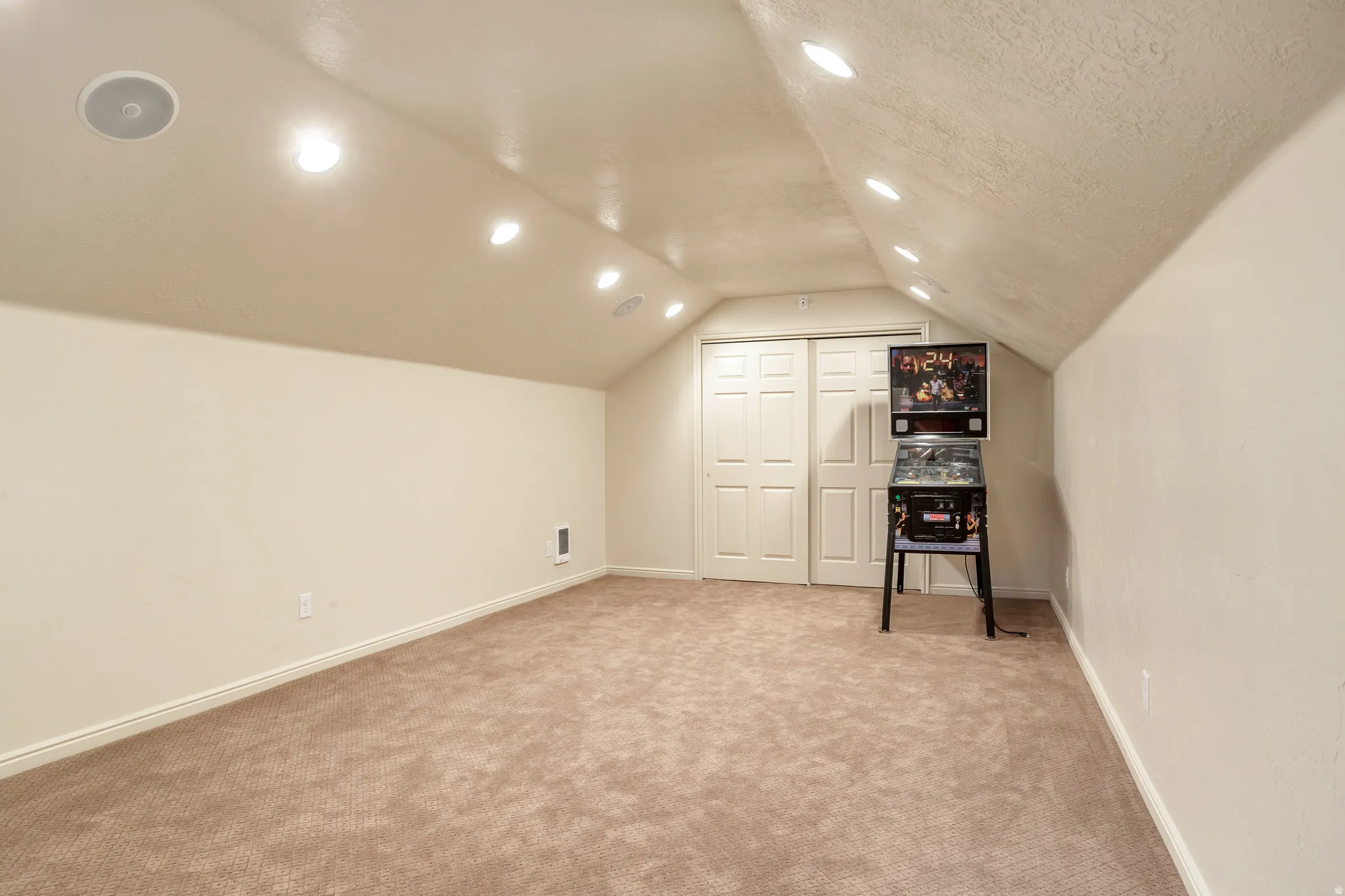 Versatile attic space featuring sloped ceilings, recessed lighting, and integrated ceiling speakers