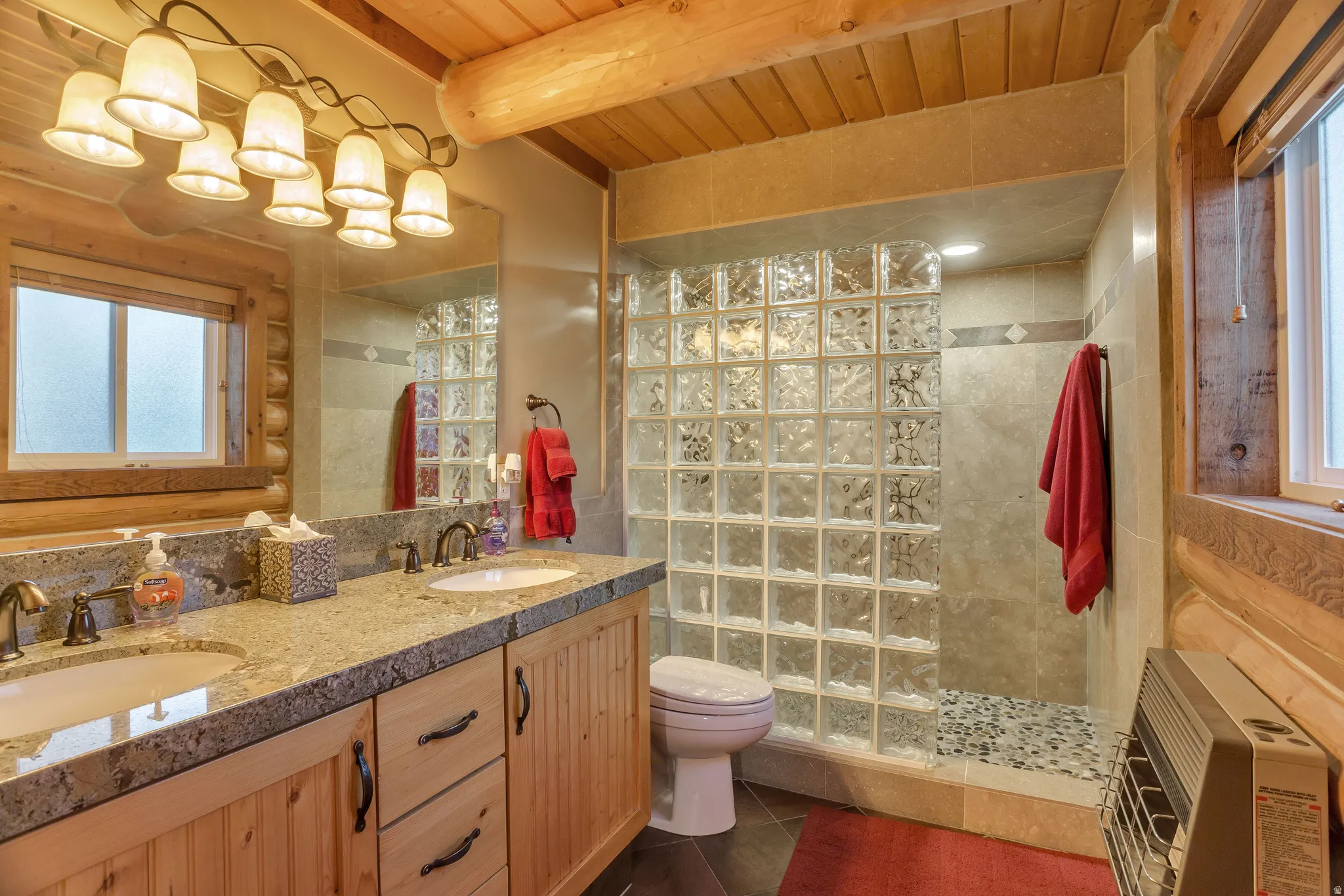 Bathroom featuring a dual vanity with a light-toned countertop, wood cabinetry, and a prominent glass block shower wall
