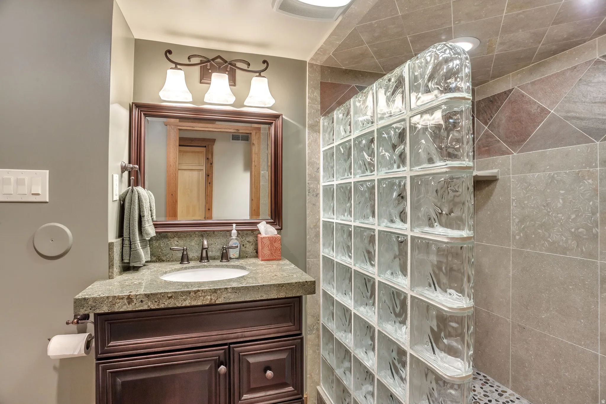 Bathroom vanity featuring a vessel sink set into a speckled countertop, framed mirror, and a three-light fixture