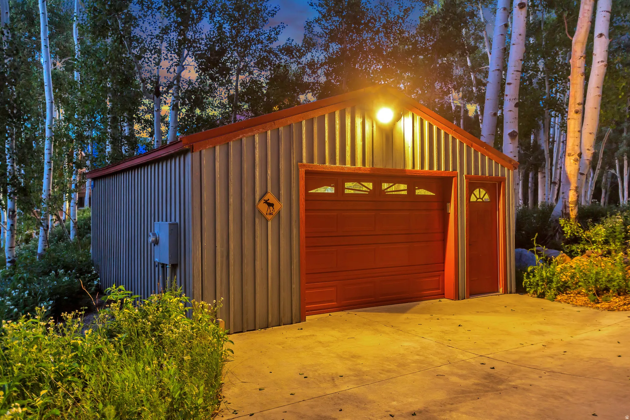 Detached corrugated metal garage featuring a red overhead door with transom windows and an adjacent red pedestrian door with a half-moon window