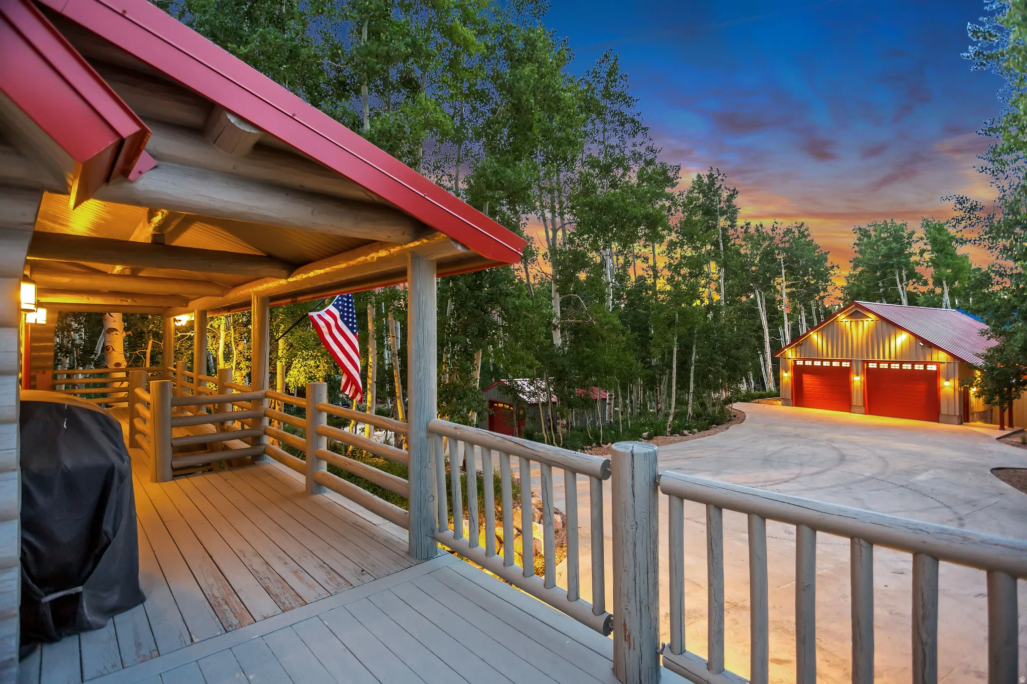 Spacious wood deck featuring log railings, a red metal roof, and wall-mounted lighting