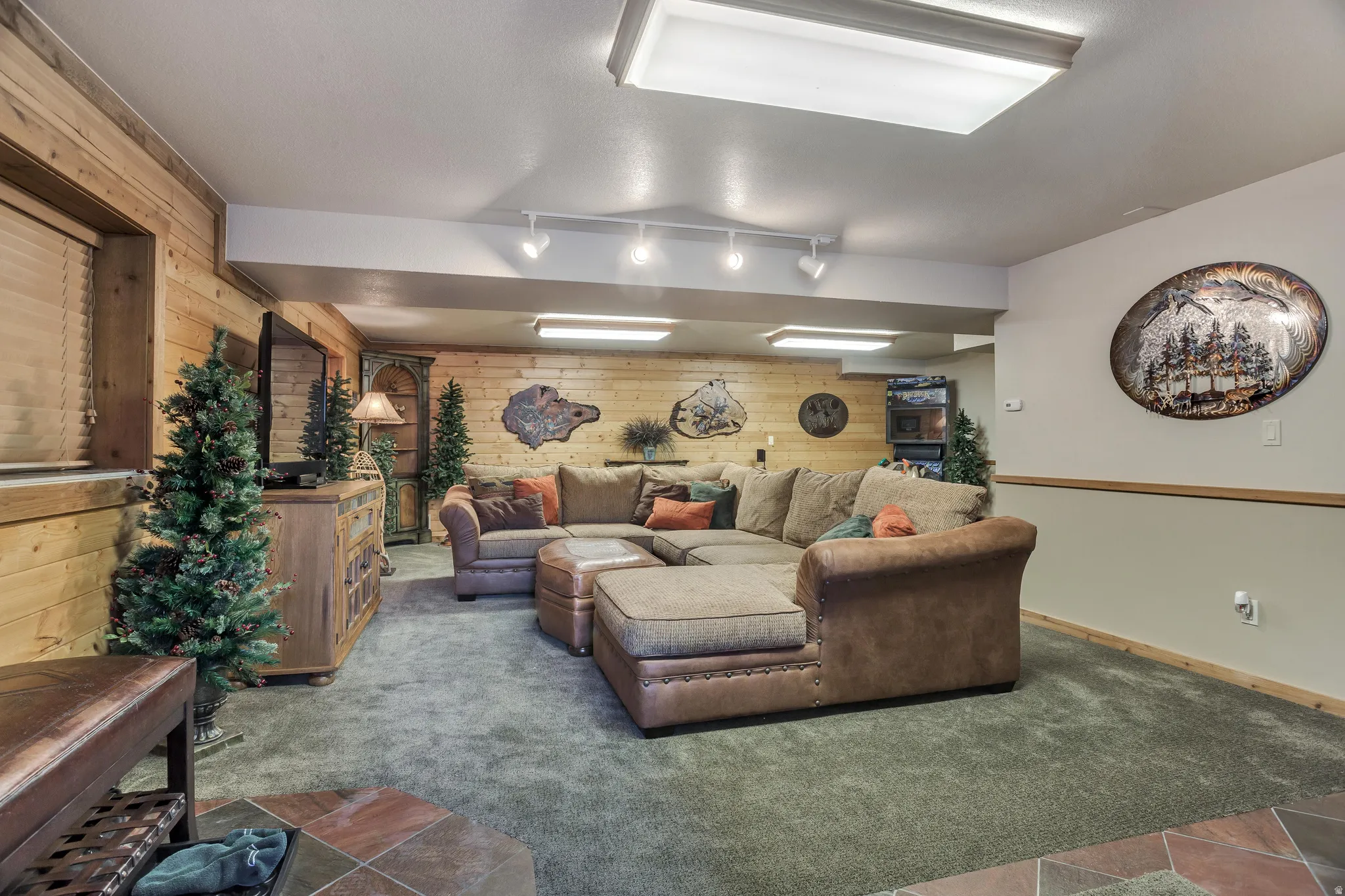 Spacious recreation room featuring wood-paneled walls, neutral carpeting, and a tiled entry floor