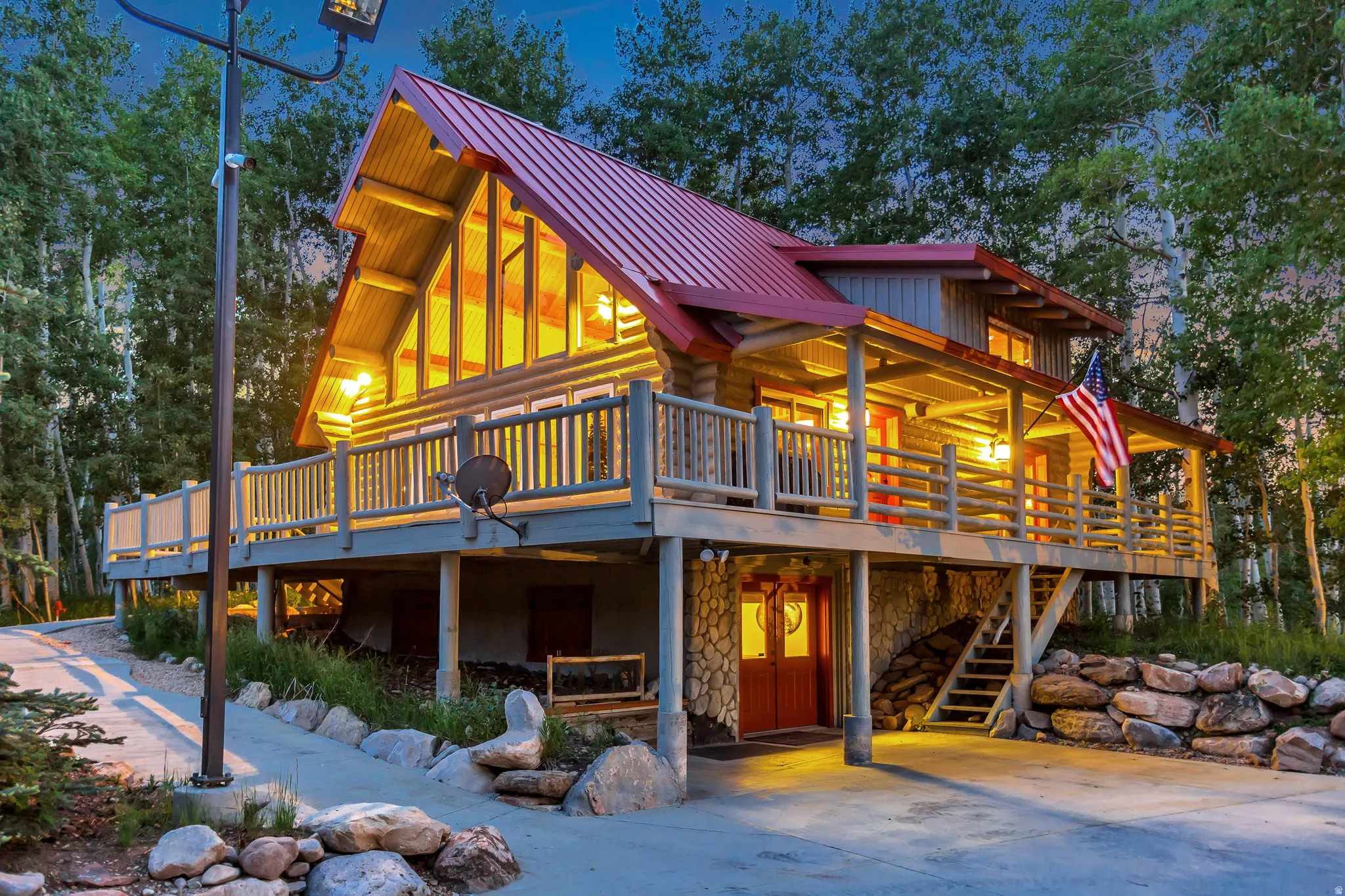 Multi-level log cabin featuring a red metal roof and extensive wood decking