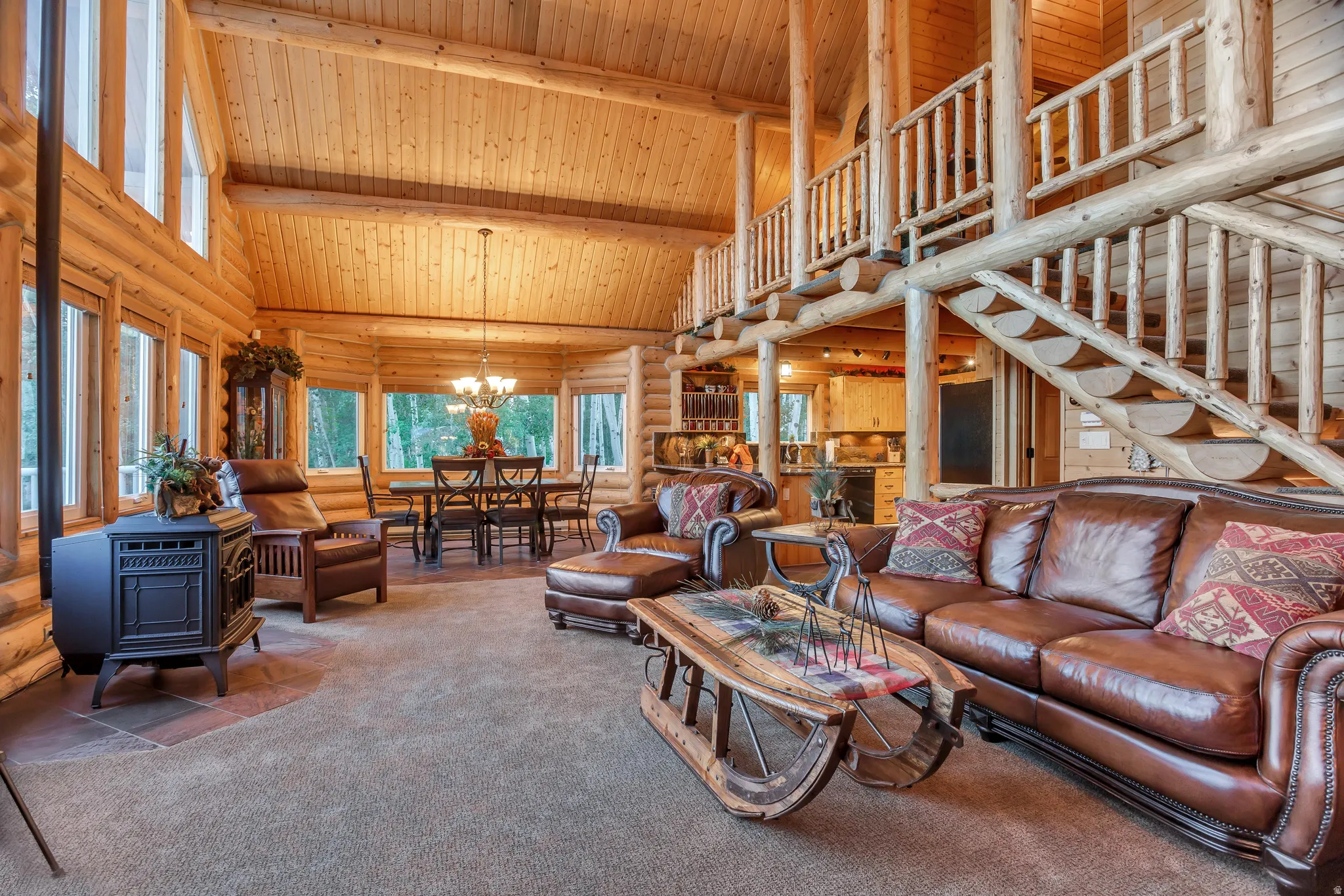 Expansive great room featuring a vaulted wood-paneled ceiling, exposed log beams, and a built-in wood staircase with log railings