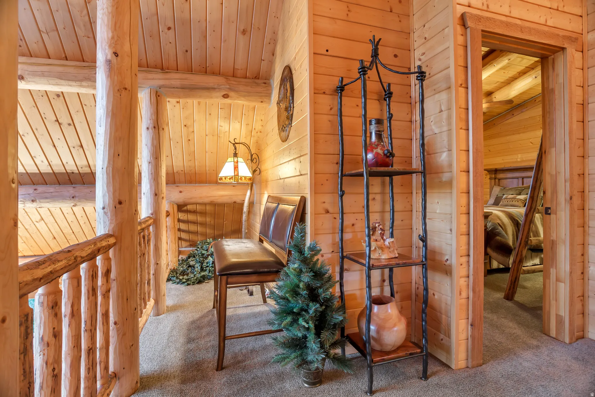 Log cabin interior featuring a wood-paneled vaulted ceiling, exposed log beams, a log railing, and carpeted flooring