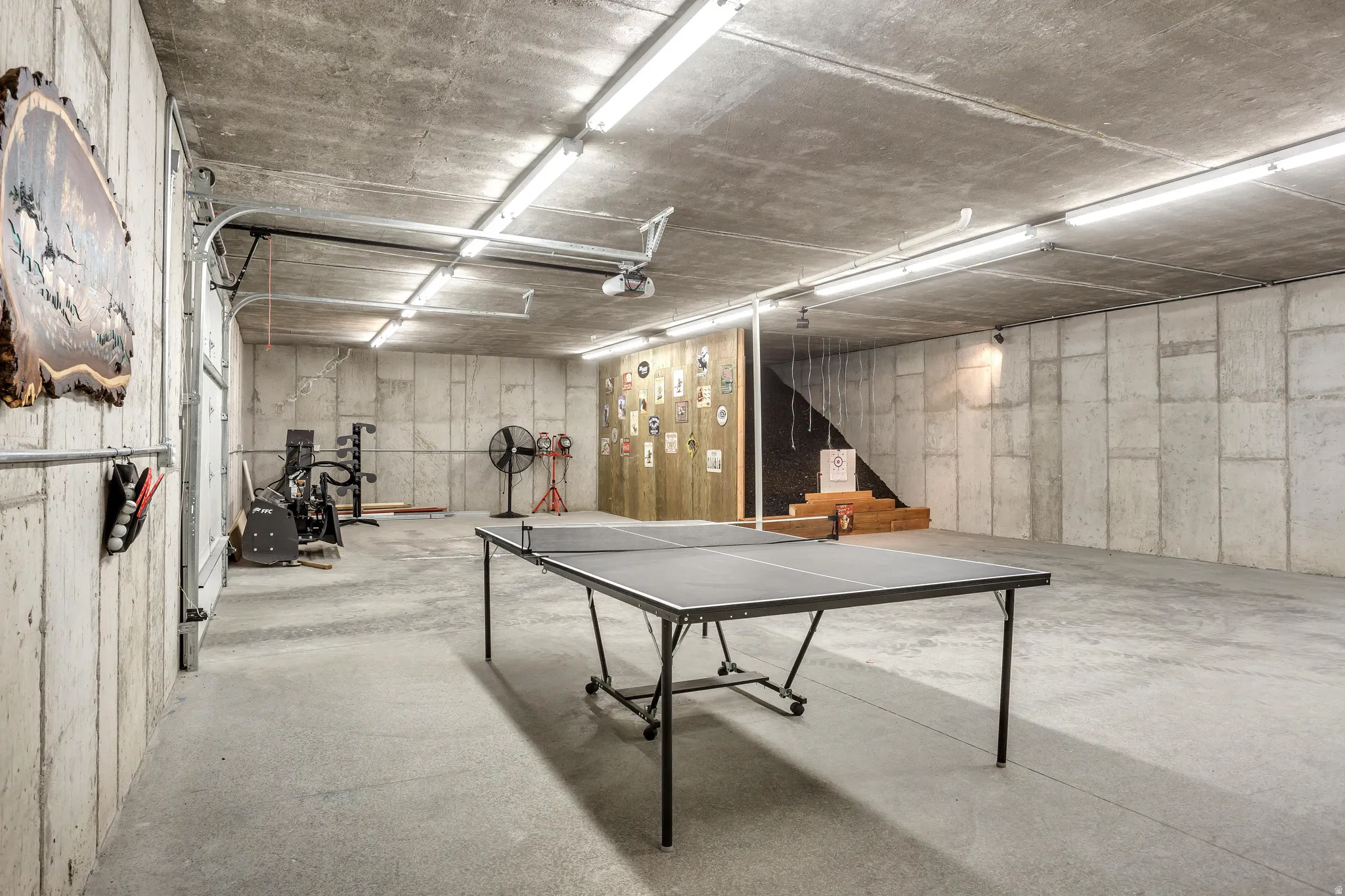 Spacious concrete-walled interior featuring an overhead garage door, industrial fluorescent lighting, and a finished concrete floor