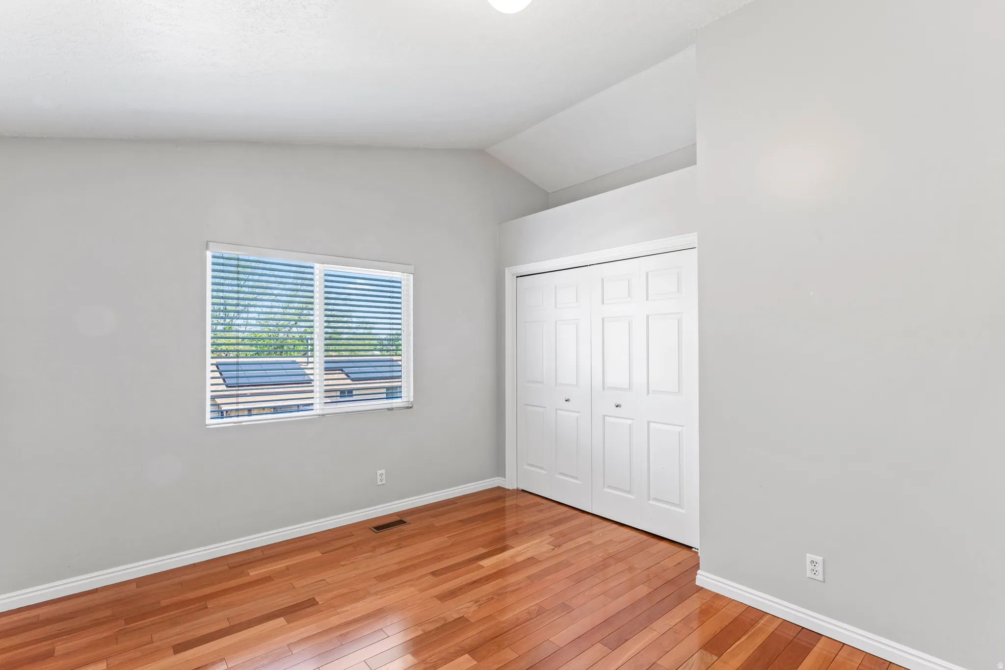 Room featuring wood-finish flooring, a window with blinds, and a built-in closet with bi-fold doors
