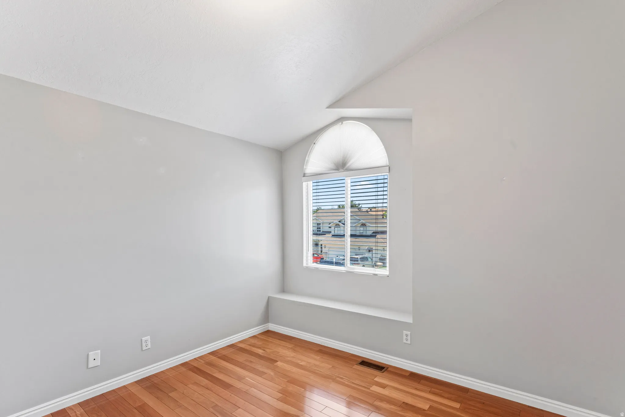 Room featuring a prominent arched window with horizontal blinds, wood-finish flooring, white baseboards, and light-colored walls