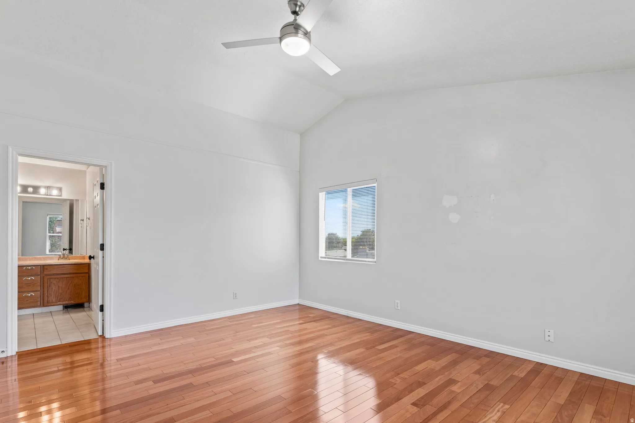Spacious room featuring wood-finish flooring, vaulted ceiling with a modern ceiling fan, and a window providing natural light