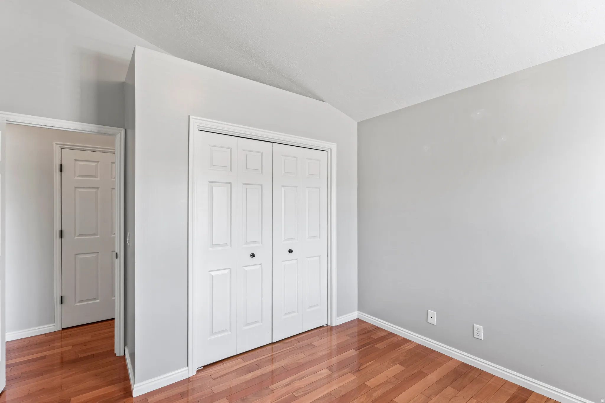 Room featuring wood-finish flooring, light grey painted walls, white baseboards, and a vaulted ceiling