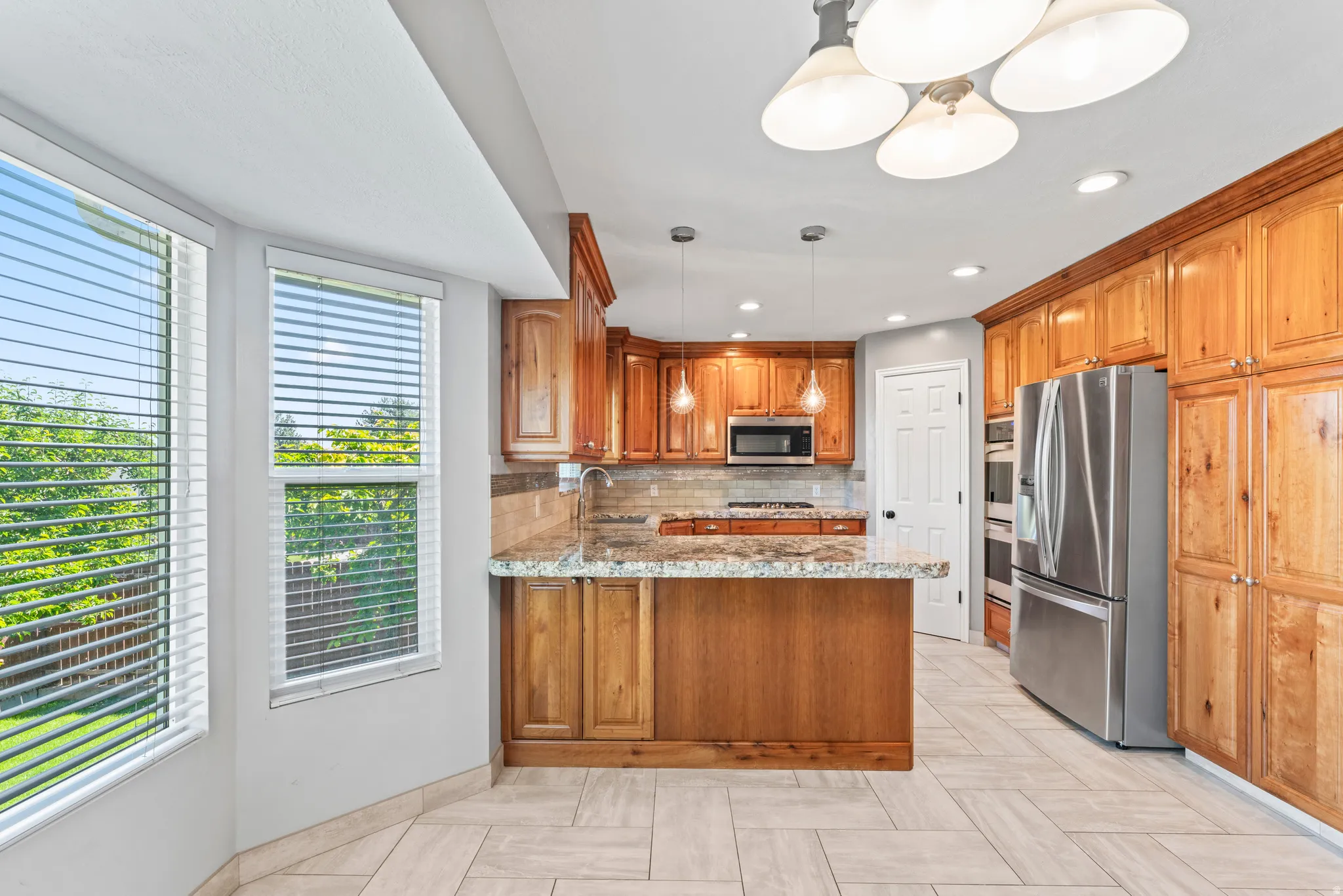 Kitchen featuring extensive wood cabinetry, stainless steel appliances, a center island with pendant lighting, stone countertops, and tile flooring