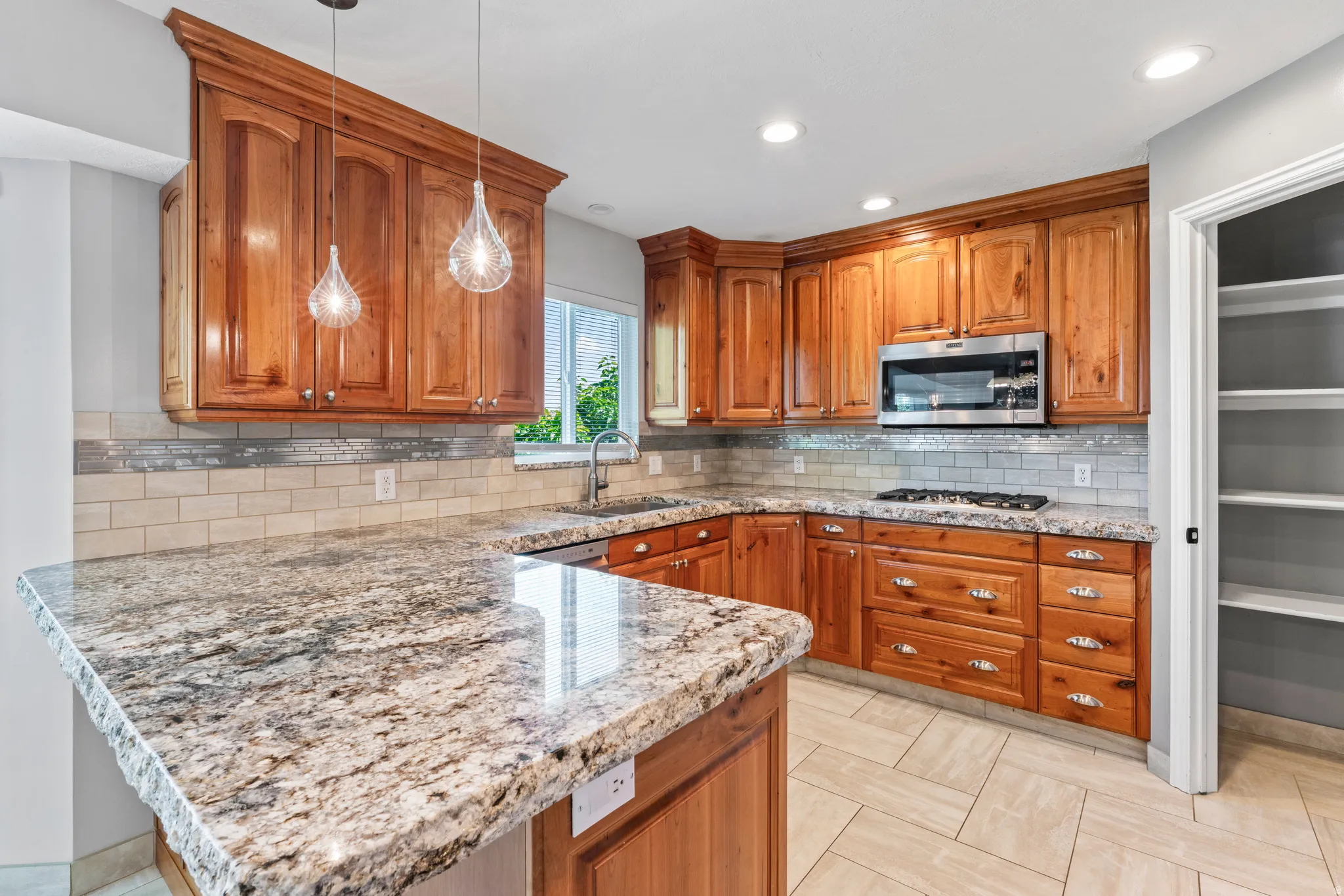 Kitchen featuring extensive wood cabinetry, speckled countertops, stainless steel microwave, tile backsplash, and recessed lighting