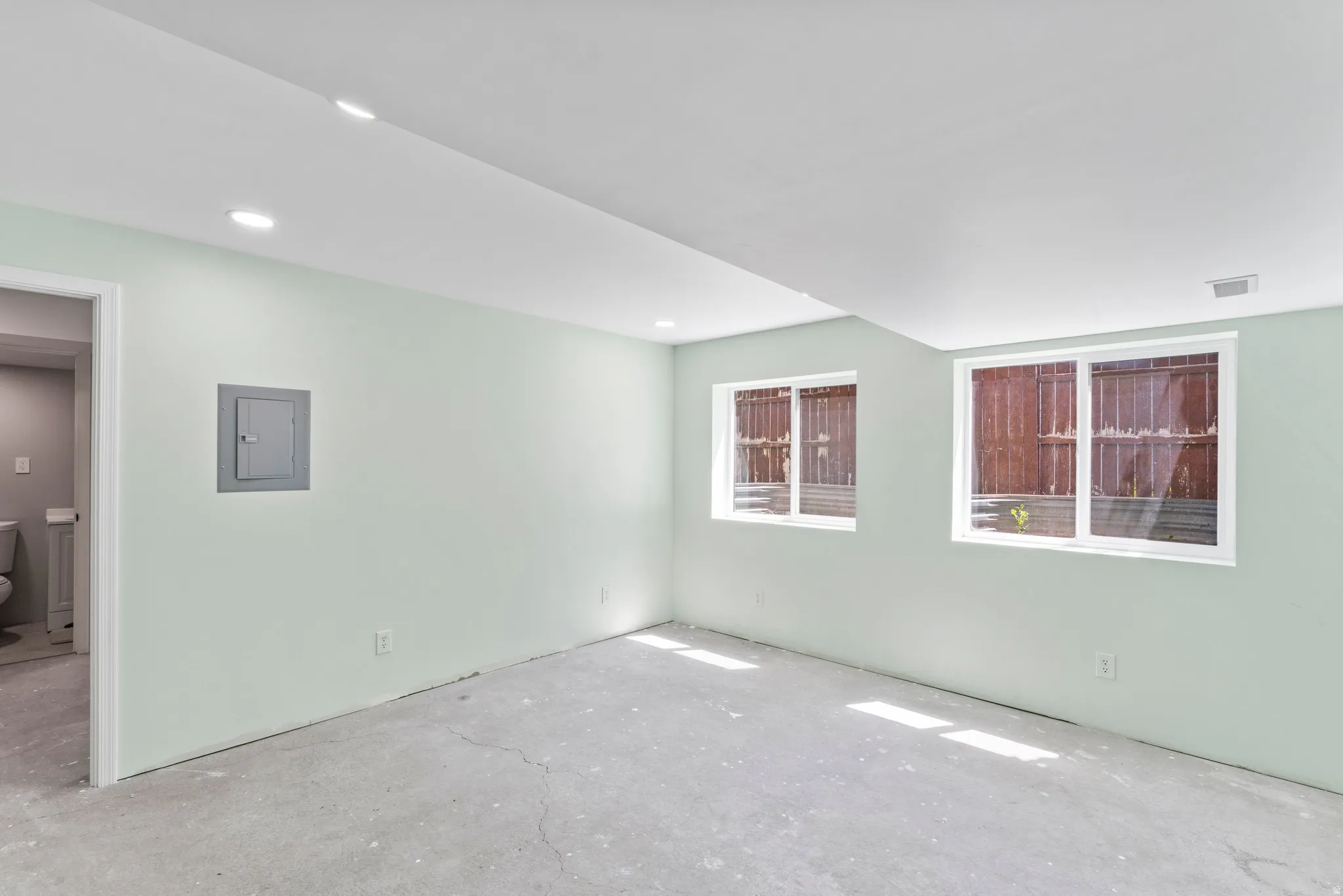 Spacious room with light green walls, recessed lighting, and two windows