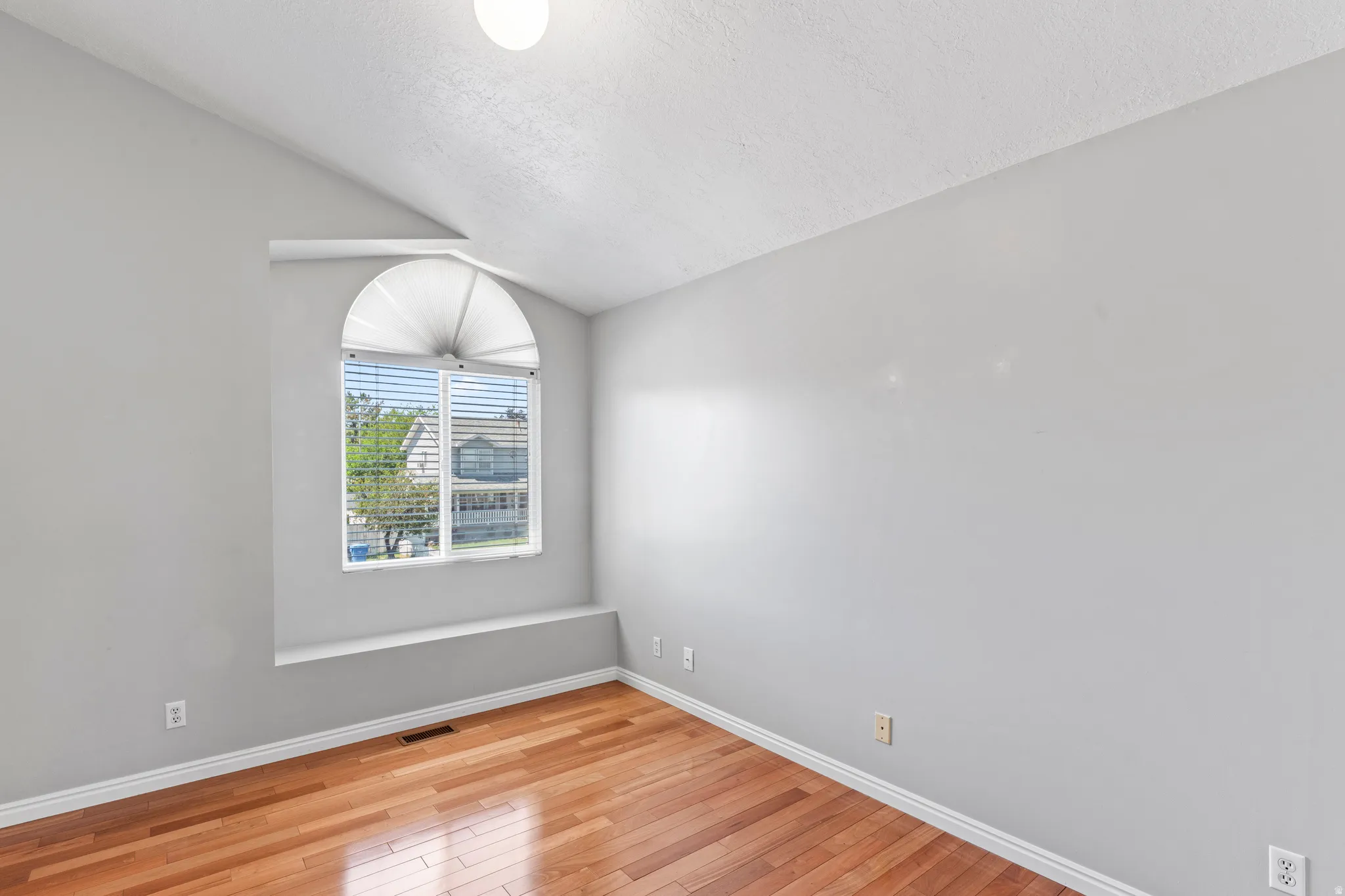 Room featuring wood-finish flooring, a vaulted ceiling, and a large arched window with horizontal blinds and a window ledge