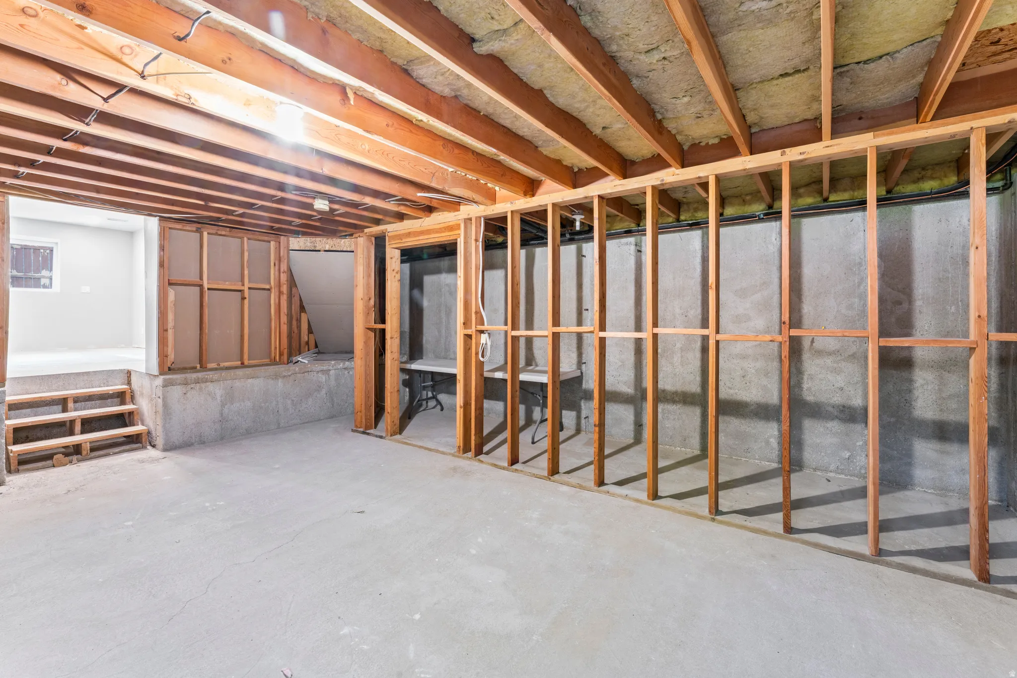 Unfinished basement space featuring exposed wood framing, concrete flooring, and visible insulation