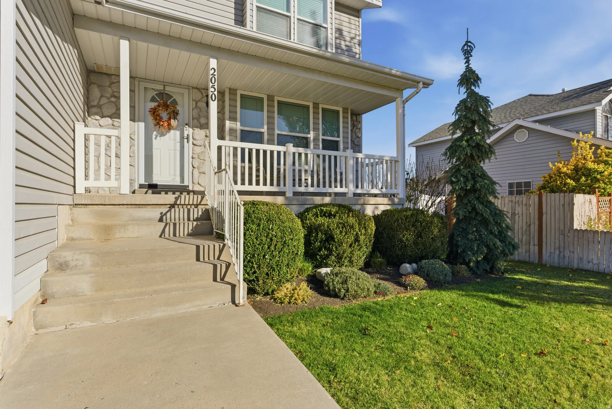 Inviting front porch with white railings, concrete steps, and stone accents